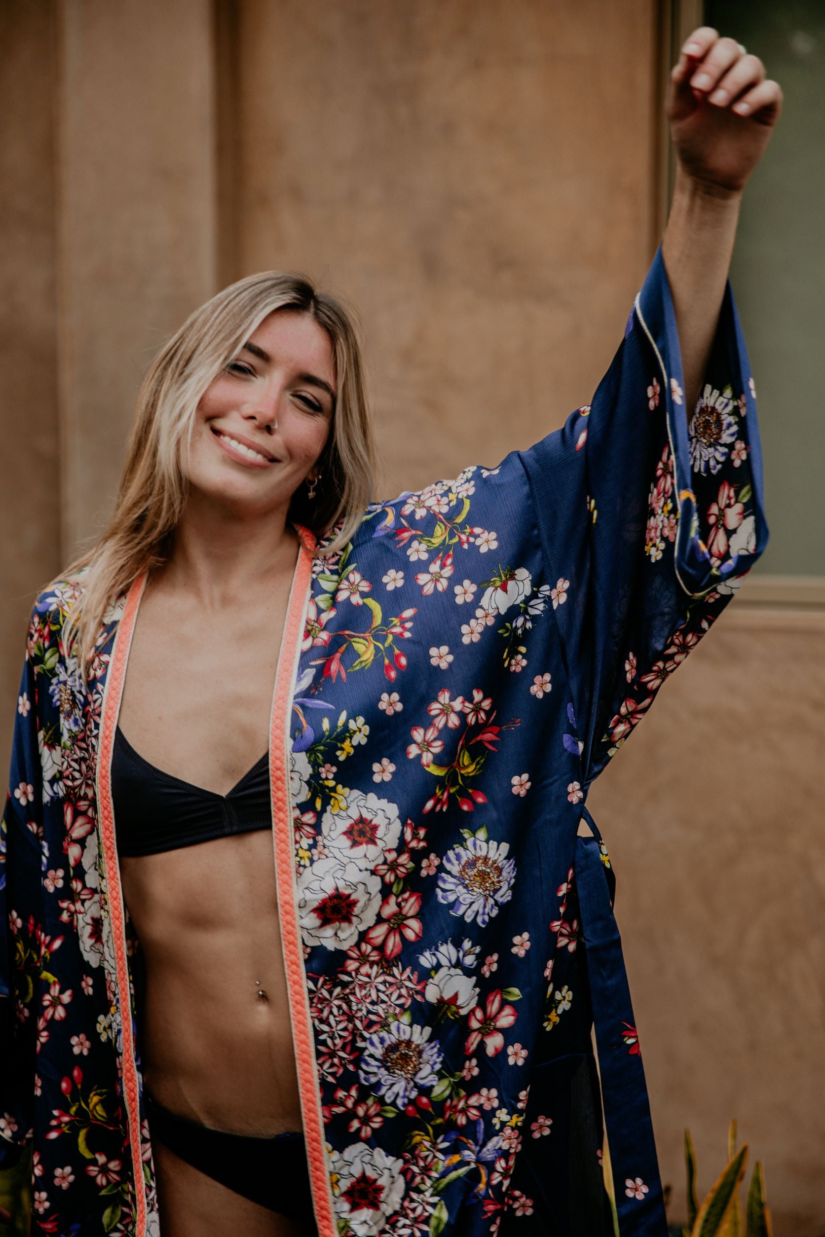 This silky kimono with wide sleeves embellished with a golden thread is gorgeous. We love the sassy side slits and the combination of the vivid flower prints and the peachy pink handwoven trim that add a pop of color and good mood.