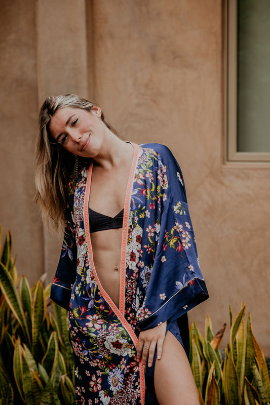 This silky kimono with wide sleeves embellished with a golden thread is gorgeous. We love the sassy side slits and the combination of the vivid flower prints and the peachy pink handwoven trim that add a pop of color and good mood.