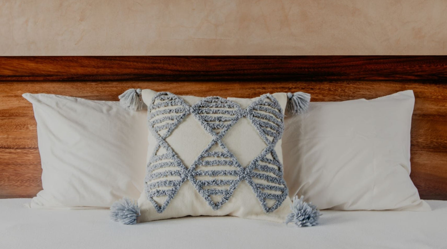 Wool yarn stitches up a textured pillow, while the geometric diamond patterns add an intriguing touch and the pom-poms add a playful feel.