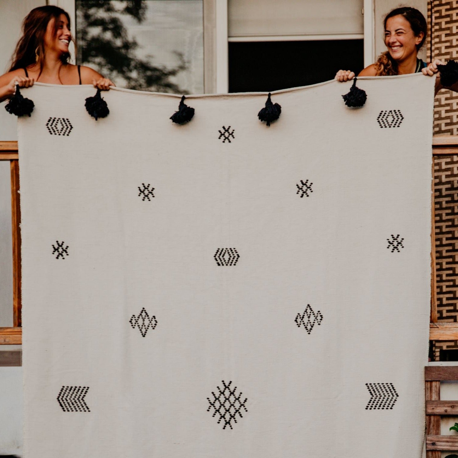 Luxurious bed or sofa cover with embroidered ethnic motifs in black against a natural neutral base finished with black pom poms. This hand-loomed cover adds an elegant, bohemian vibe to your bedroom.