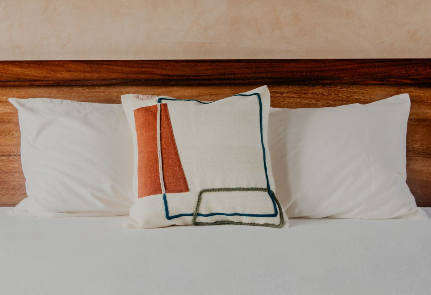 Asymmetric and colourful wool designs float across the ivory space of this beautiful pillow. Hand-loomed by expert artisans, the different shapes embroidered in wool bring an artsy look and extra coziness to your bed, sofa or chaise.