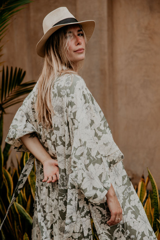 This silky kimono with wide sleeves embellished with a golden thread is gorgeous. We love the sassy side slits and the combination of flower prints and the soft green and white colors that grant a bohemian vibe to this kimono. The neckline is enhanced by an elegant handwoven trim.
