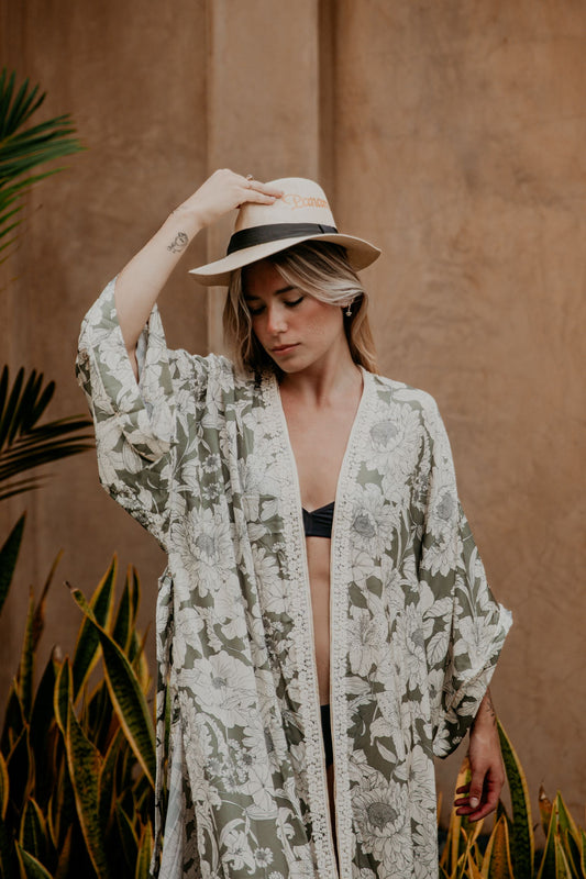 This silky kimono with wide sleeves embellished with a golden thread is gorgeous. We love the sassy side slits and the combination of flower prints and the soft green and white colors that grant a bohemian vibe to this kimono. The neckline is enhanced by an elegant handwoven trim.