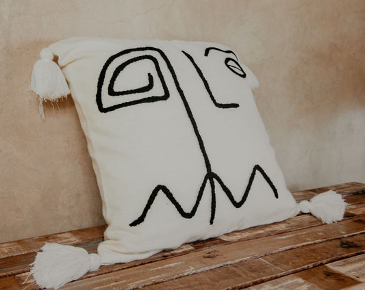 Hand-loomed pillow and embroidered by skilled artisans with a geometric face inspired by the Cubism movement stitched on a cream ground finished with white pom poms.