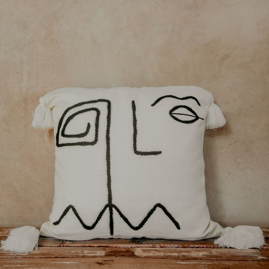 Hand-loomed pillow and embroidered by skilled artisans with a geometric face inspired by the Cubism movement stitched on a cream ground finished with white pom poms.