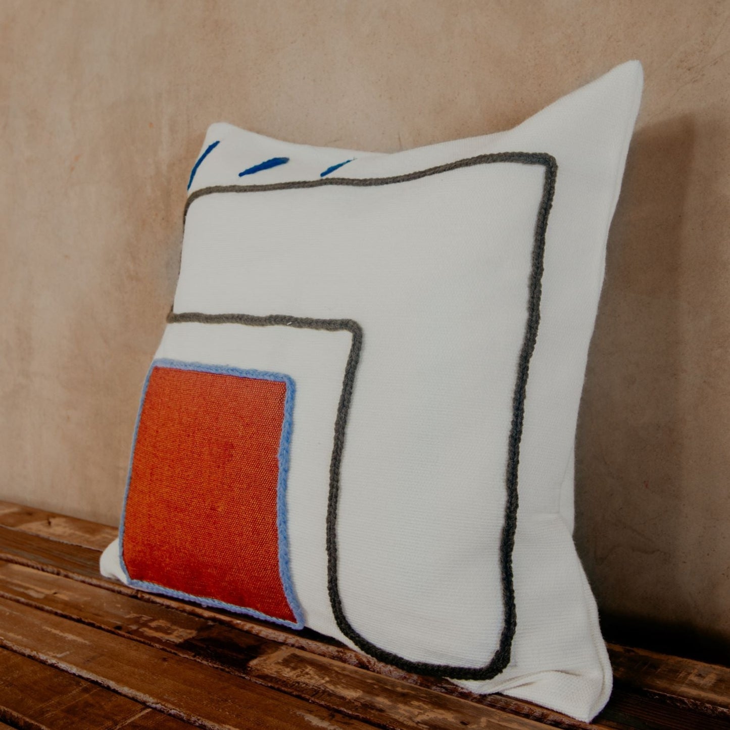 Asymmetric and colourful wool designs float across the ivory space of this beautiful pillow. Hand-loomed by expert artisans, the different shapes embroidered in wool bring an artsy look and extra coziness to your bed, sofa or chaise.