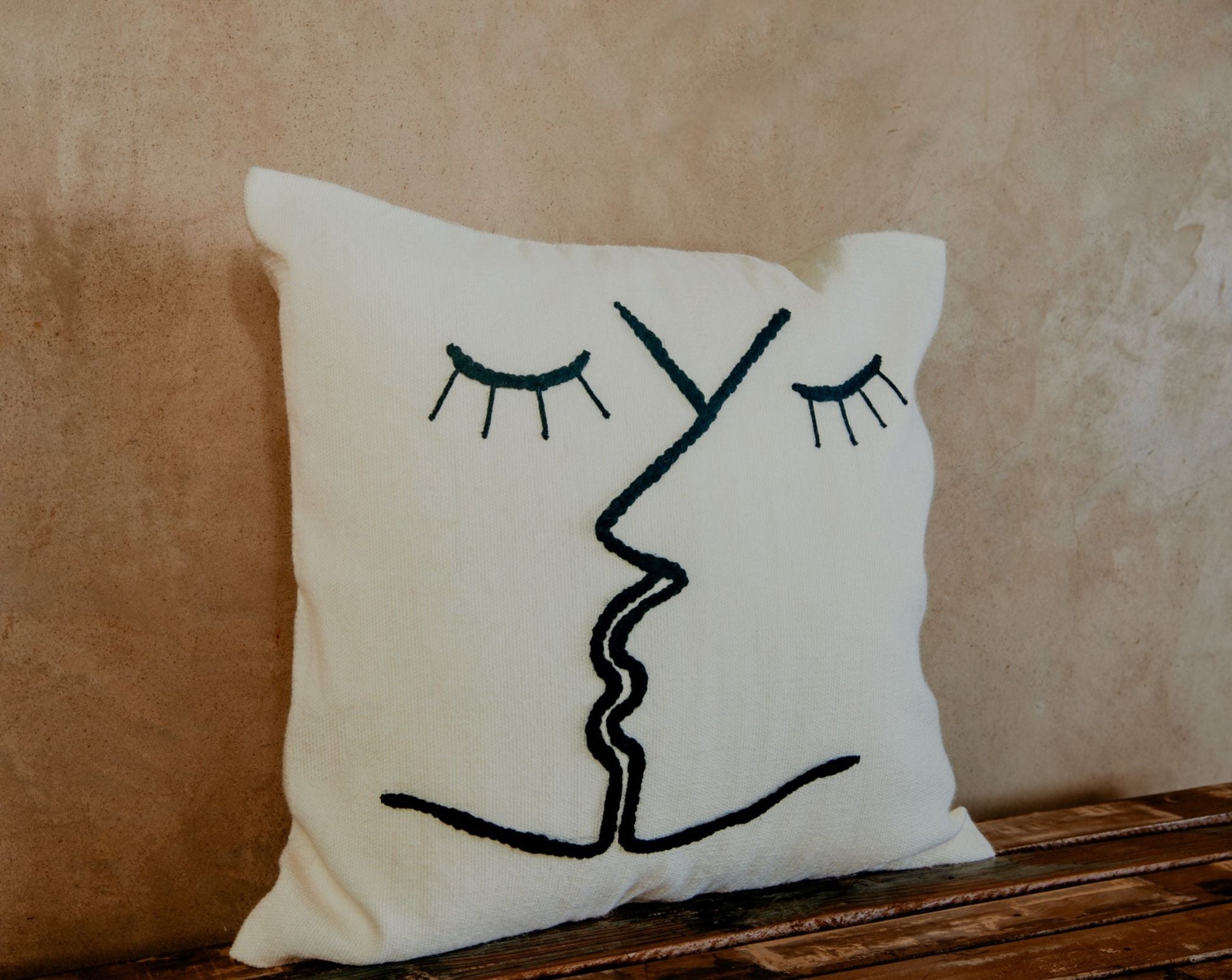 You will love this look-good, feel-good pillow. Hand-loomed and embroidered by skilled artisans with two kissing faces stitched on a cream ground